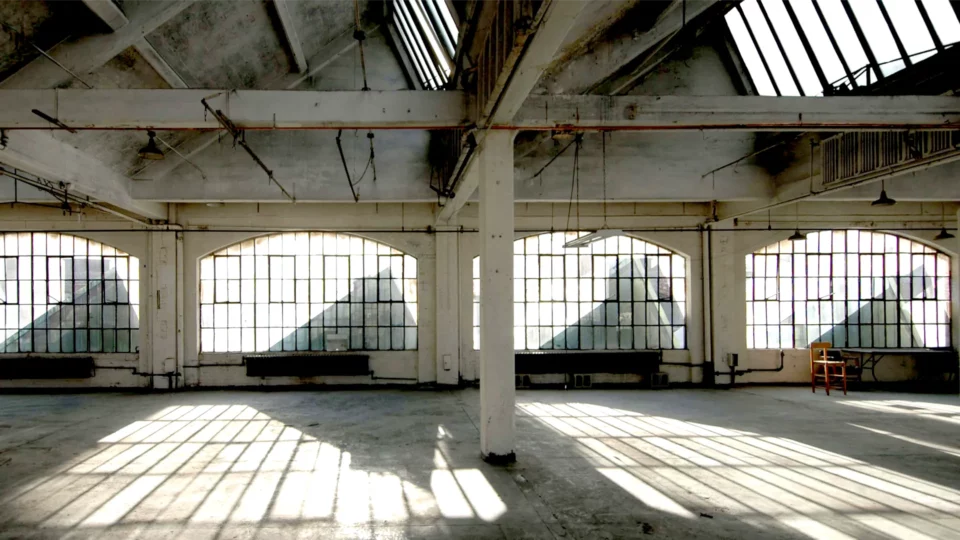Large industrial space with skylight windows and dramatic lighting casting shadows. Campaign by PlanetFab Studio.