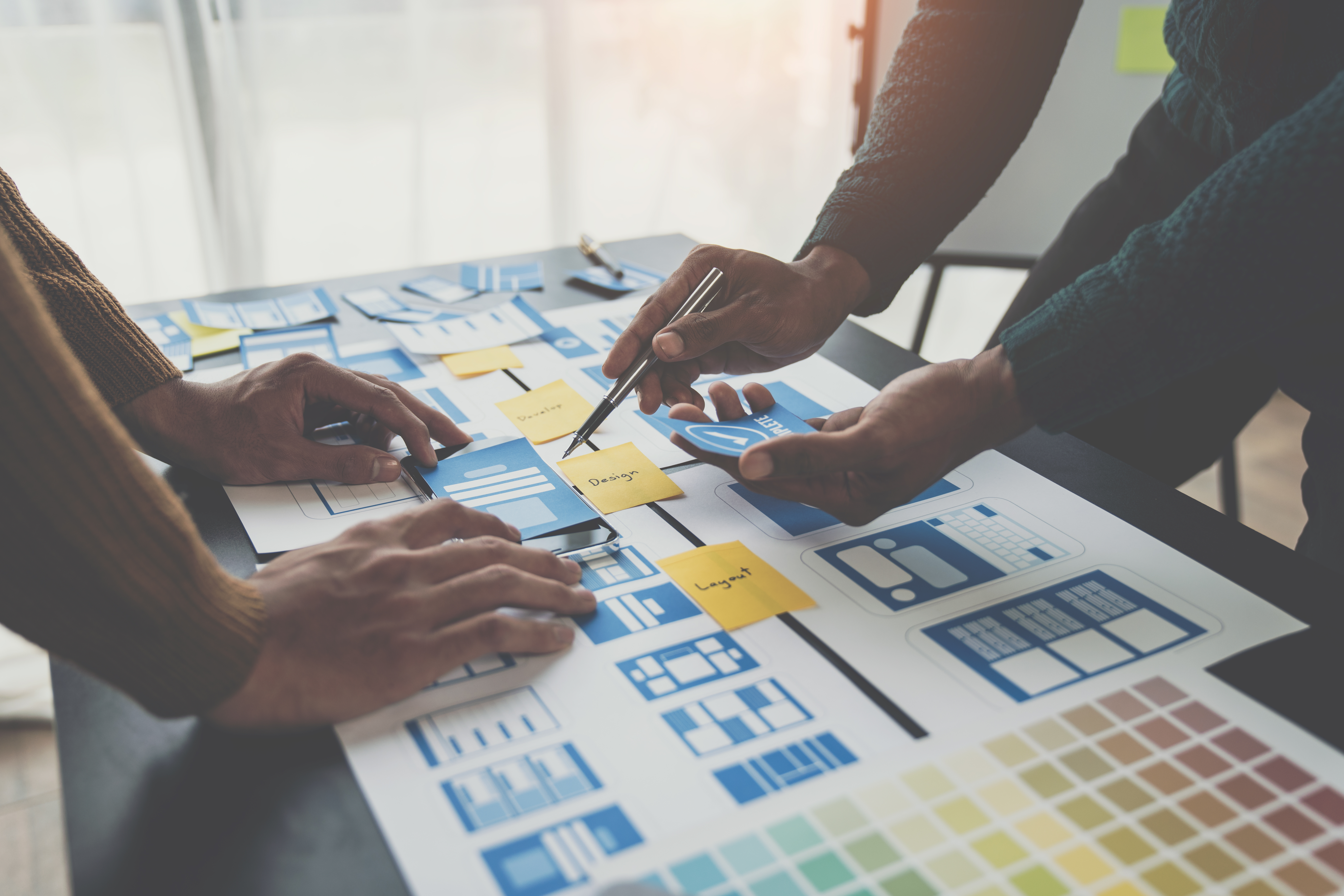 Hands of web designers arranging wireframes and sticky notes during a collaborative site redesign planning session.