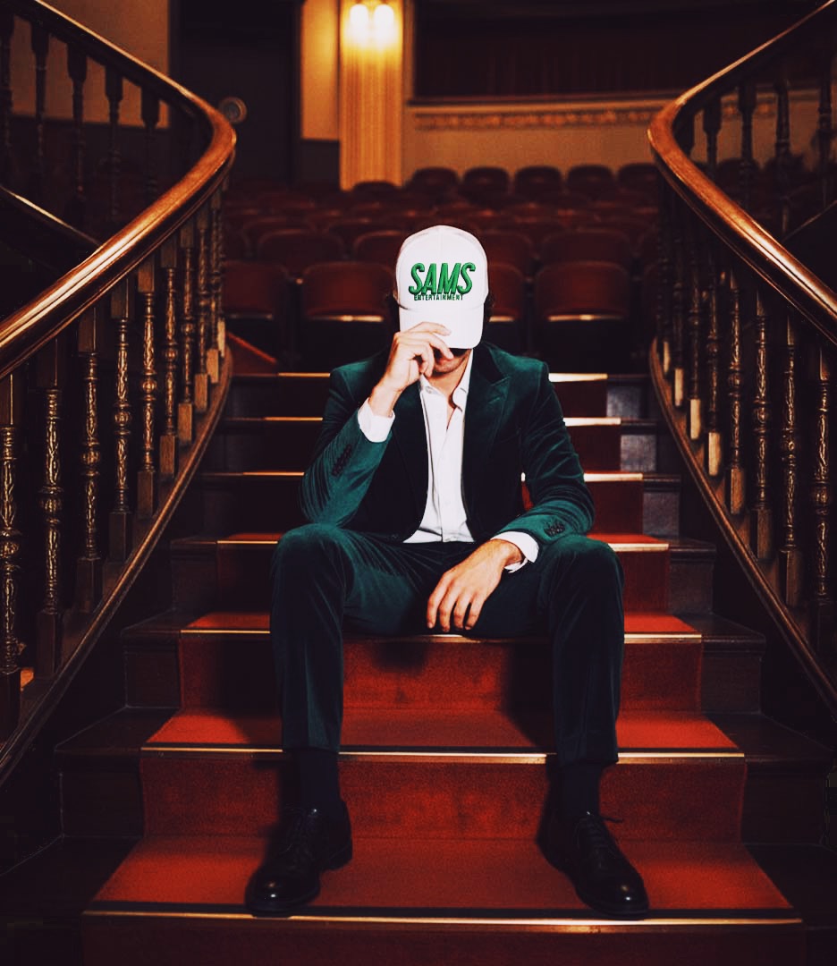 Man wearing Sams Entertainment branded hat seated on Broadway theater stairs