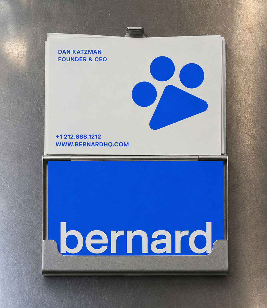 Bernard AI business card holder showing front and back card designs — white card with paw print logo and founder contact details, and royal blue card with white Bernard wordmark. Bernard AI brand identity by PlanetFab.