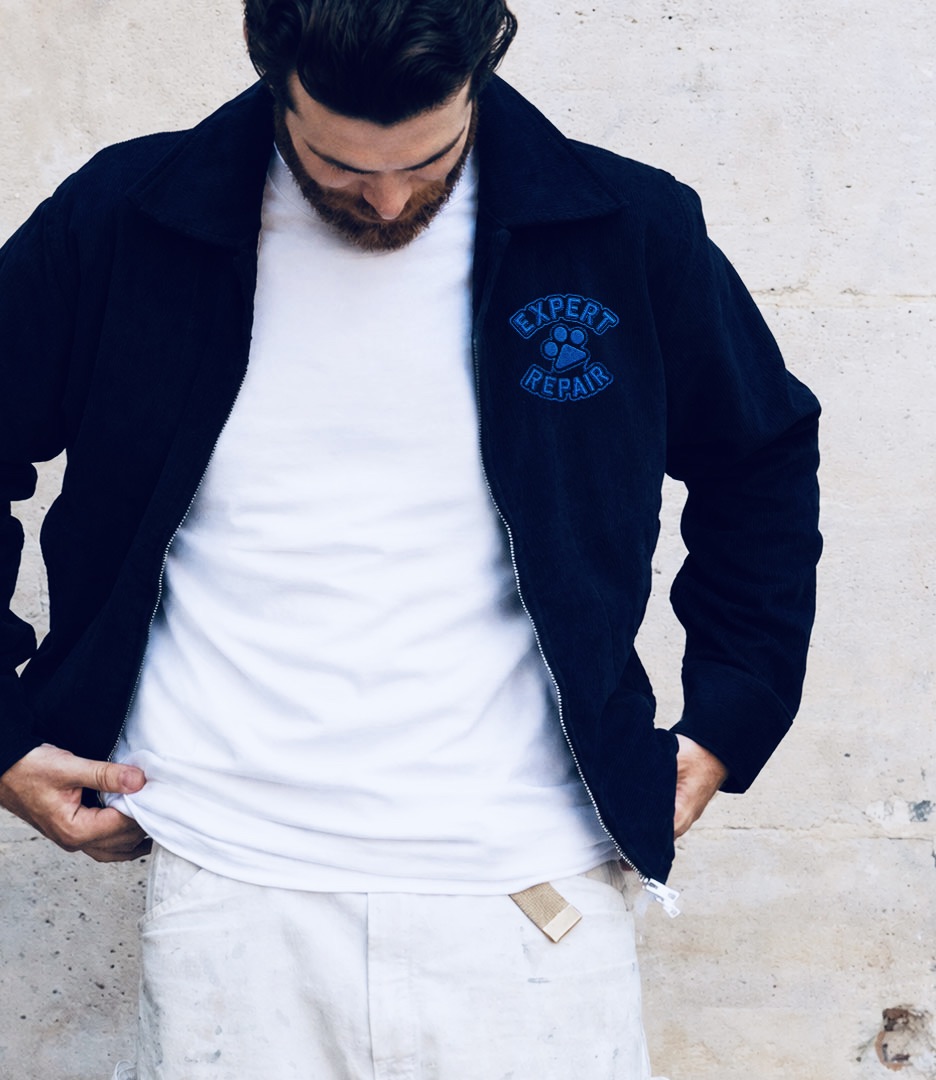 Man wearing a navy work jacket with an Expert Repair embroidered patch featuring the Bernard paw print logo. Bernard AI brand identity by PlanetFab.