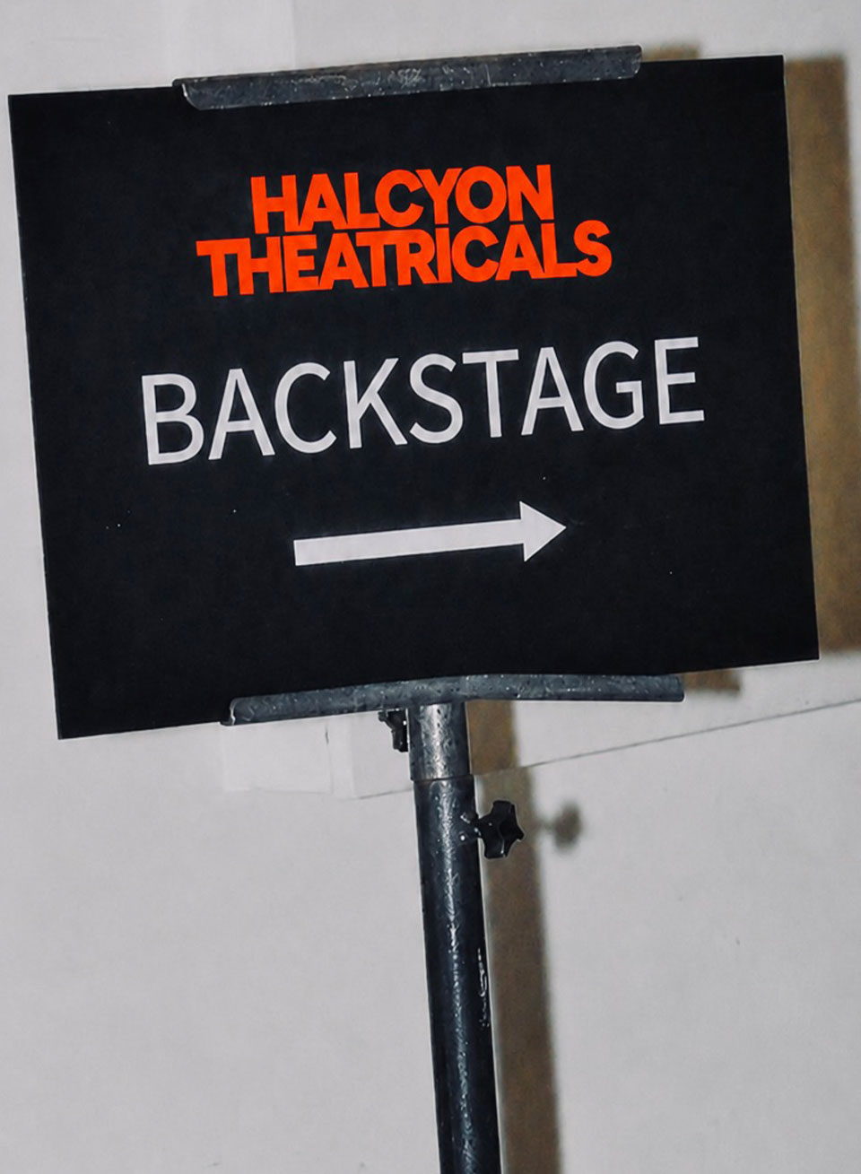 Halcyon Theatricals backstage directional sign featuring the red wordmark, white BACKSTAGE lettering and arrow.
