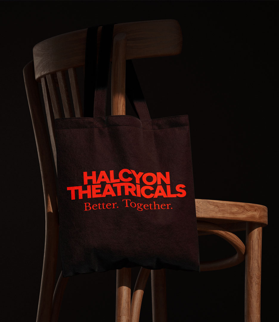 Dark brown Halcyon Theatricals tote bag featuring the red wordmark and Better. Together. brand message, displayed on a wooden chair.